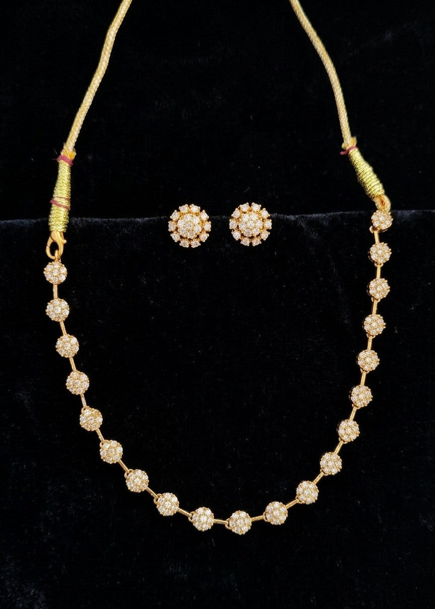 Gold-toned jewelry set featuring a beaded necklace and matching stud earrings displayed on a black velvet surface.