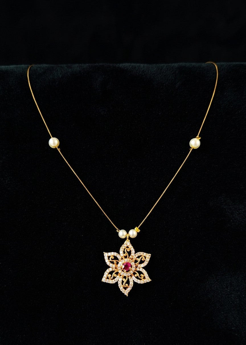 A gold necklace with a floral pendant and small pearl beads, displayed on a black velvet jewelry bust.