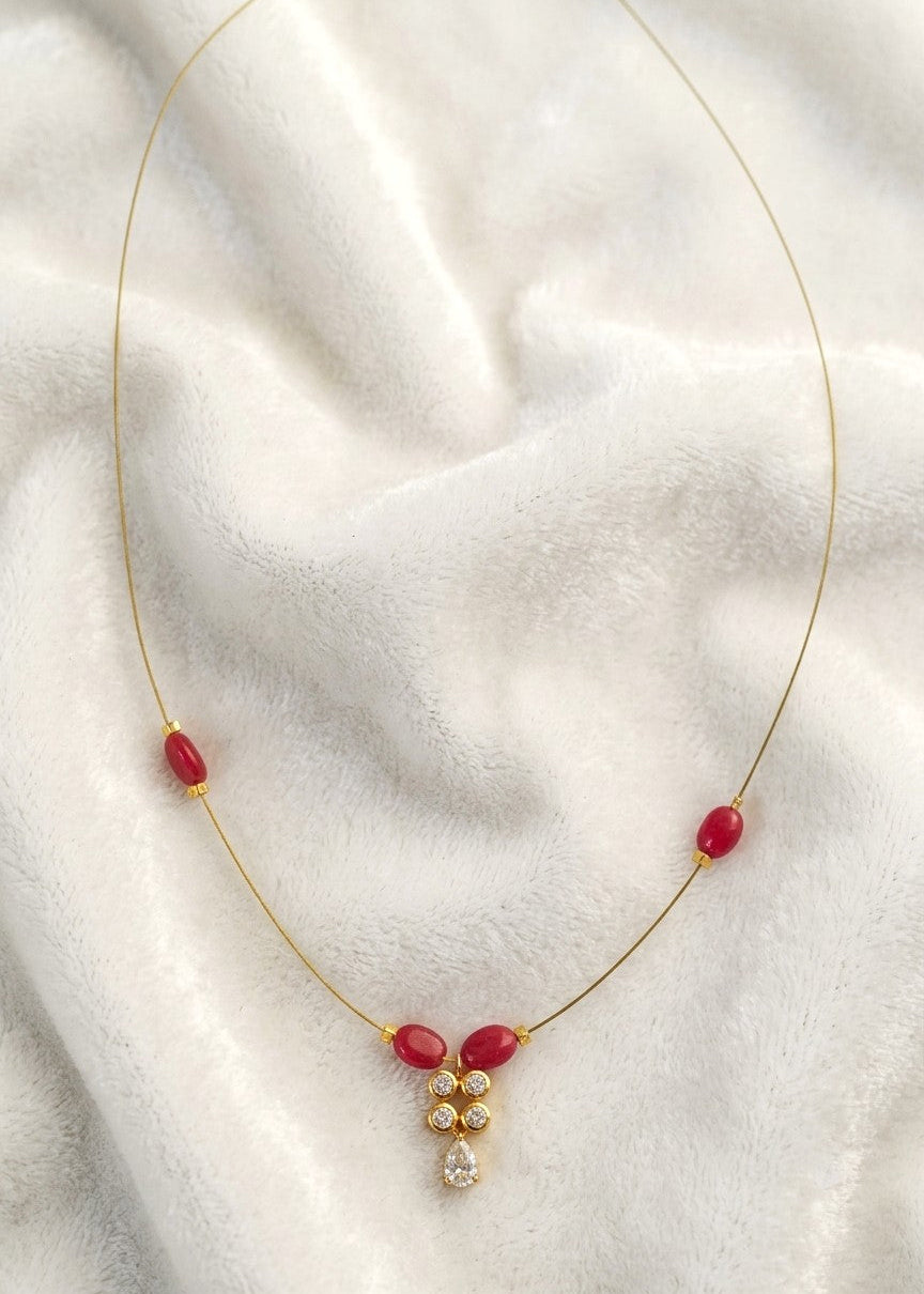 Kashish necklace on a white display, showing ruby-red oval beads and a delicate crystal teardrop pendant.