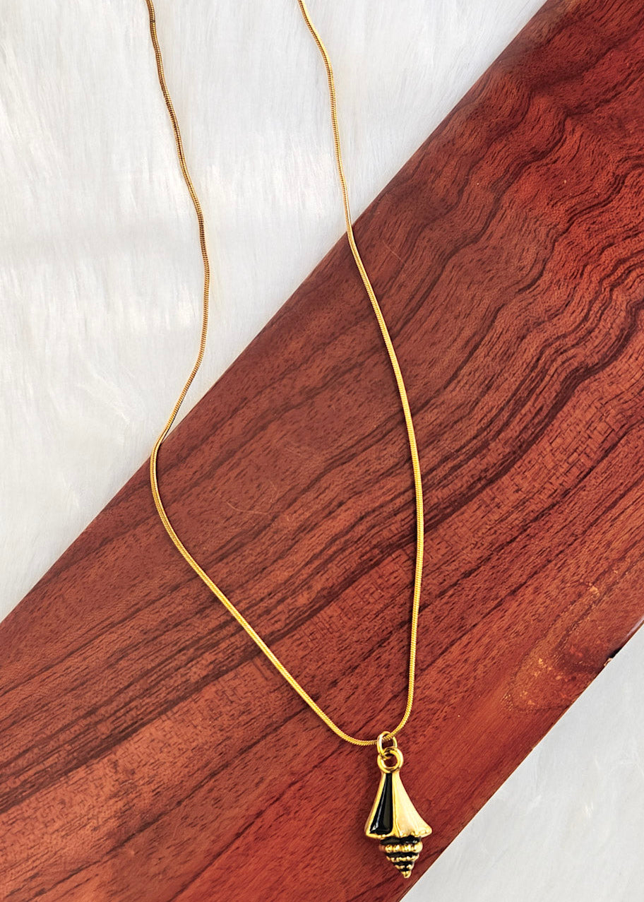 A gold chain necklace with a small gold pendant, displayed on a diagonal wooden block over a white textured background.