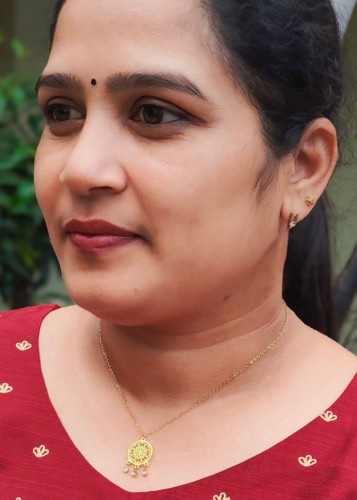 A close-up portrait of a woman wearing a gold anti-tarnish pendant necklace with a small decorative charm,
