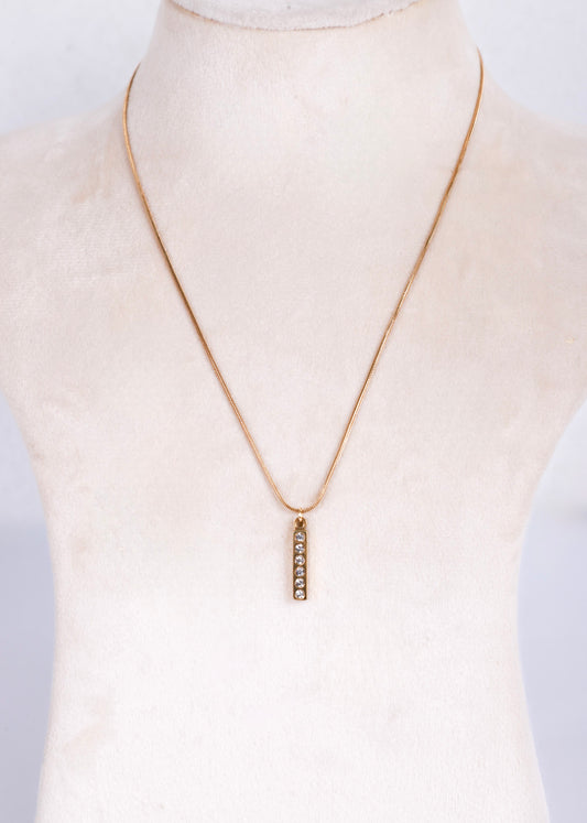 A delicate antish tarnish gold chain necklace with a small vertical bar pendant set with clear stones, displayed on a cream-colored mannequin bust.