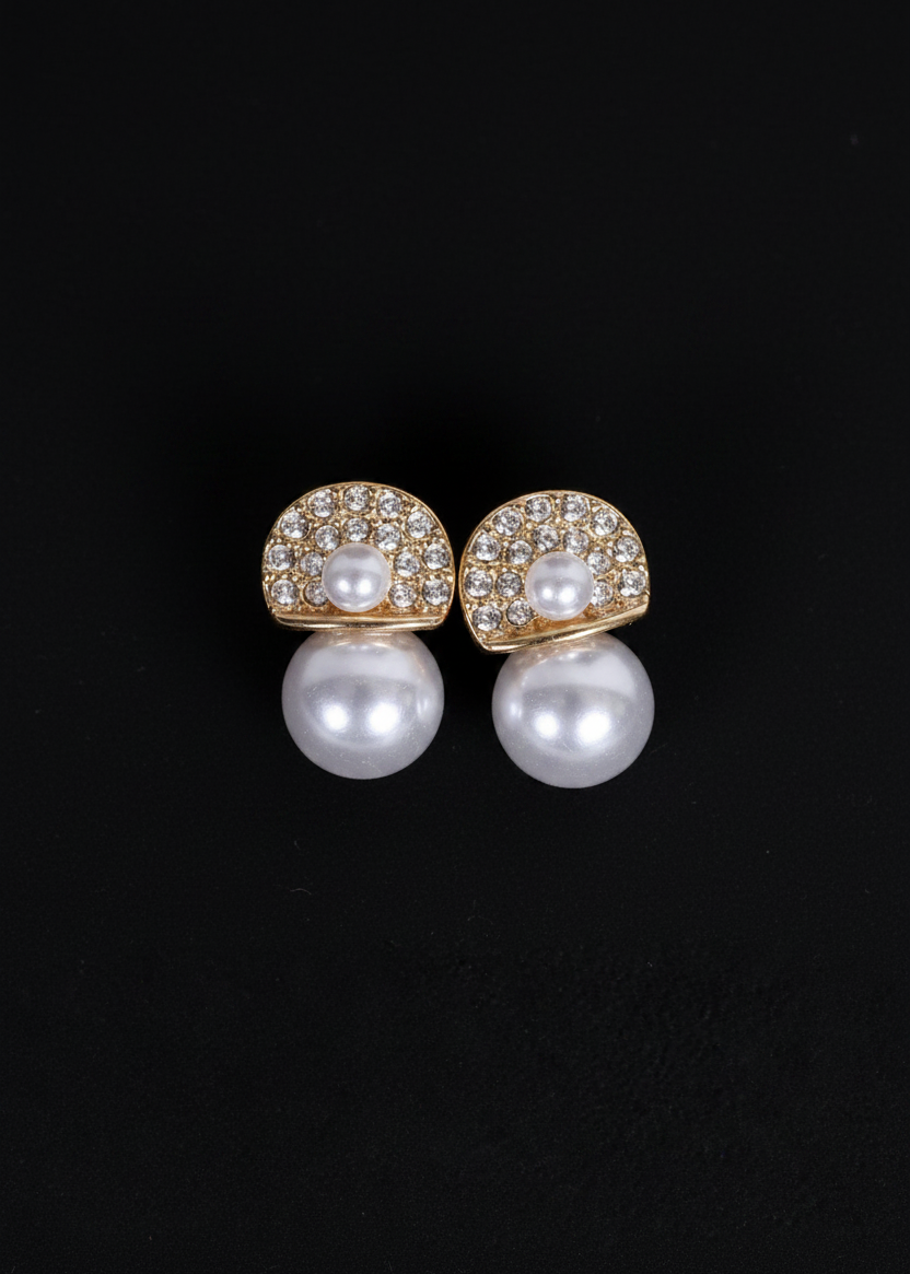 A pair of gold and pearl stud earrings with pavé-set clear stones, shown on a solid black background.