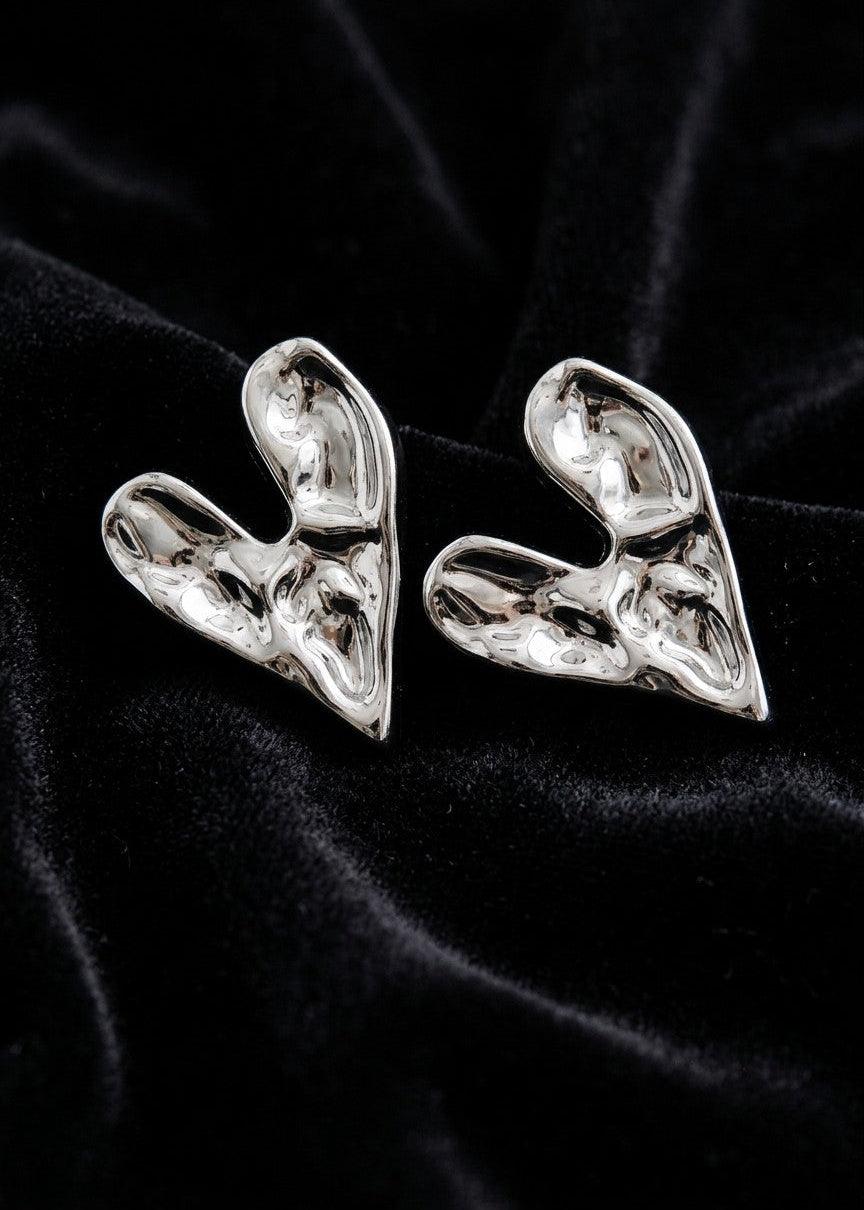 A pair of chunky, sculptural silver earrings with a highly textured, organic, fluid-like surface, displayed on a black velvet fabric background.