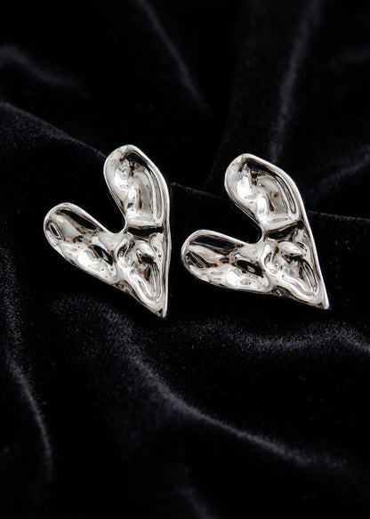 A pair of chunky, sculptural silver earrings with a highly textured, organic, fluid-like surface, displayed on a black velvet fabric background.