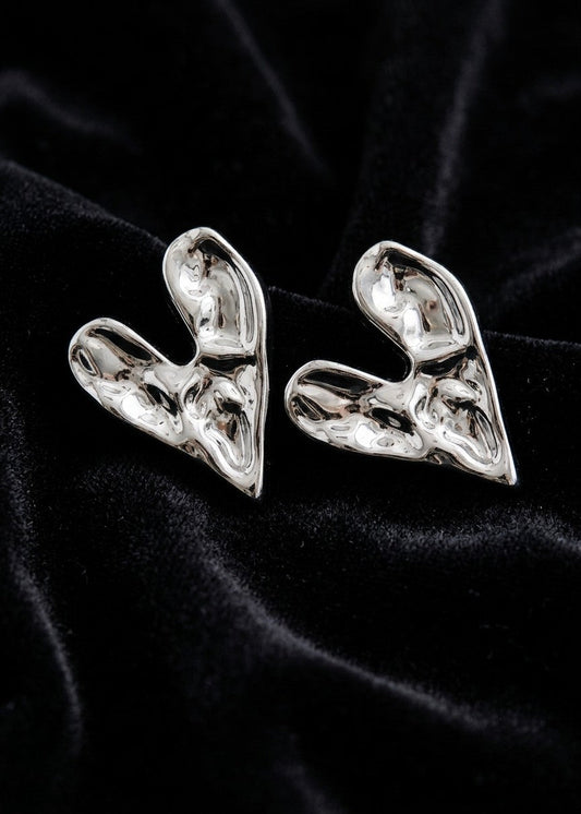 A pair of chunky, sculptural silver earrings with a highly textured, organic, fluid-like surface, displayed on a black velvet fabric background.