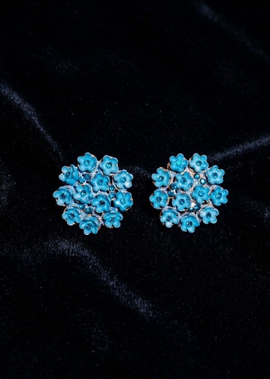 A pair of round turquoise blue floral stud earrings with silver-toned metal settings, displayed on a black velvet background.