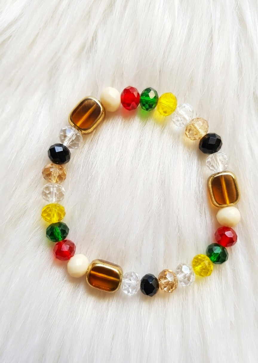 A beaded stretch bracelet featuring a mix of red, green, yellow, black, clear, and brown beads, displayed on a white faux fur background.