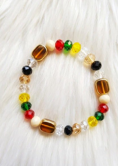 A beaded stretch bracelet featuring a mix of red, green, yellow, black, clear, and brown beads, displayed on a white faux fur background.