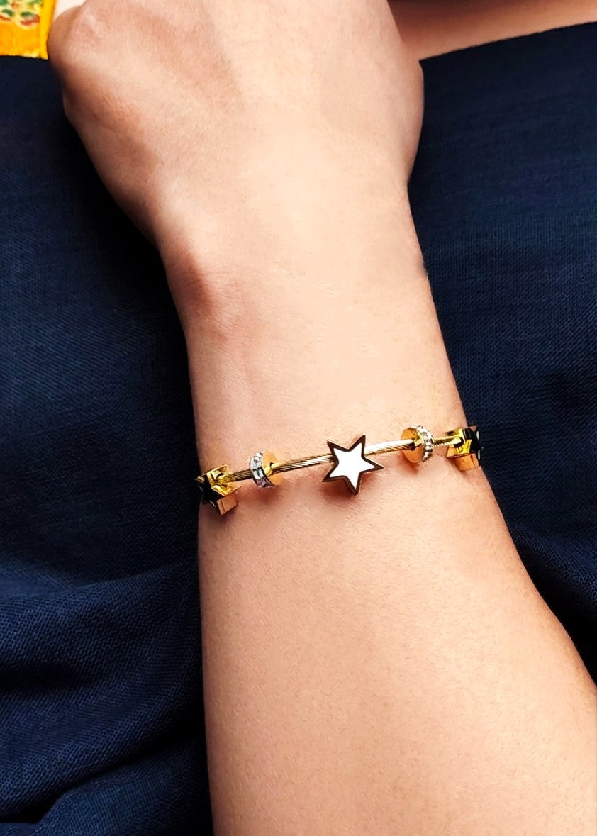 A close-up of a person's wrist wearing a gold-plated charm bracelet with a central silver star charm and small gold and silver beads.