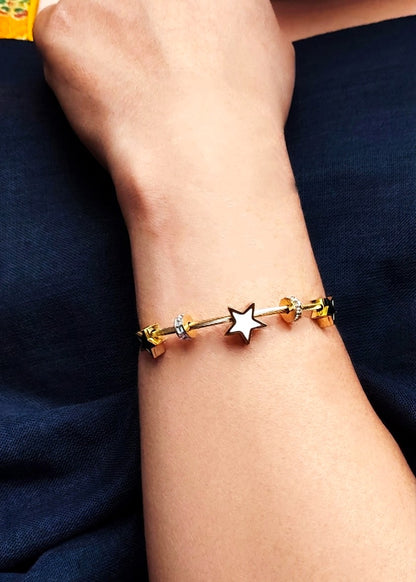 A close-up of a person's wrist wearing a gold-plated charm bracelet with a central silver star charm and small gold and silver beads.