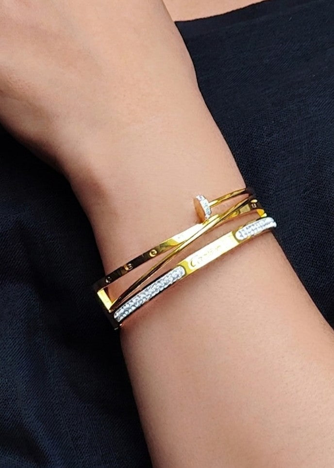 A close-up of a person's wrist wearing a stack of three slim bangle bracelets. Two bracelets are gold-toned, and one is silver-toned with a row of small clear stones.