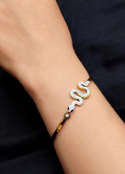 A close-up of a person's wrist wearing a silver snake bracelet with clear rhinestones, set against a dark navy blue background.