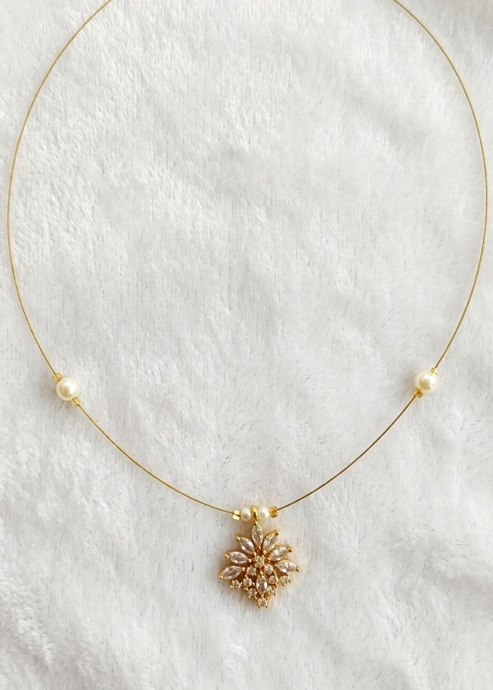 A delicate gold necklace with a central floral cluster pendant and two small pearl beads on either side, displayed on a soft white textured fabric background.