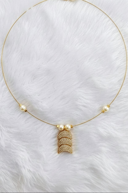 A delicate gold necklace with three small white pearls spaced along the chain and a central gold pendant featuring textured stacked crescent shapes, displayed on a white faux fur background.