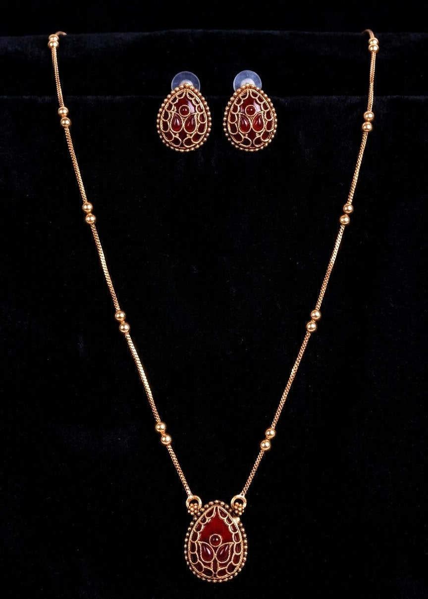 Gold-toned jewelry set featuring a beaded necklace with a teardrop pendant and matching stud earrings, decorated with red enamel and white floral detailing, displayed on a black velvet background.