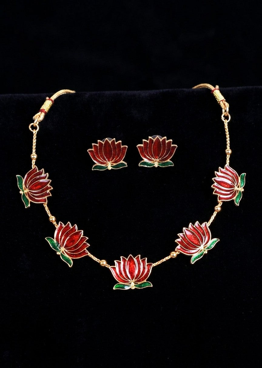 Gold-tone jewelry set featuring a necklace and matching earrings with red lotus flower motifs and green leaves, displayed on a black velvet background.