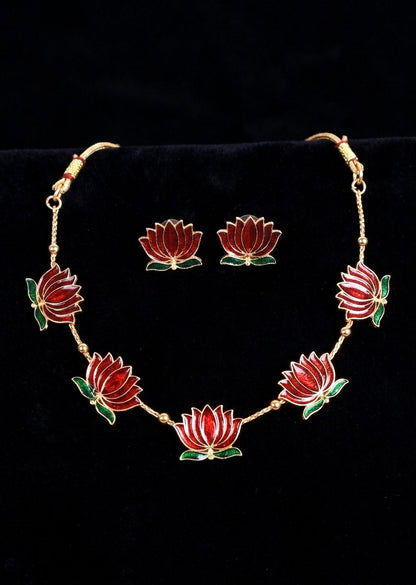 Gold-tone jewelry set featuring a necklace and matching earrings with red lotus flower motifs and green leaves, displayed on a black velvet background.