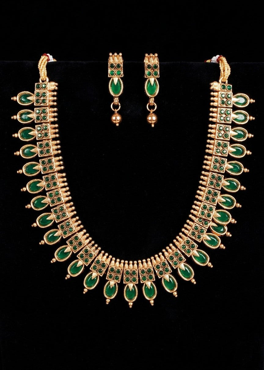 Gold-plated traditional Indian jewelry set featuring a necklace and matching earrings with green stone accents, displayed on a black background.