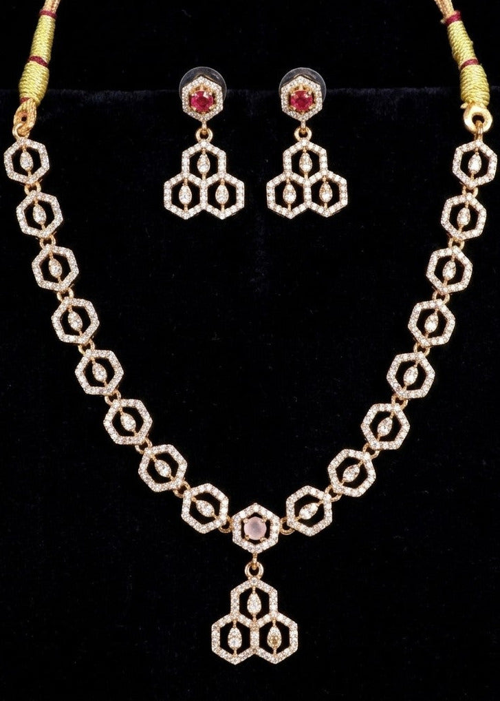 Gold-toned traditional necklace and matching drop earrings with repeating geometric hexagonal motifs and small red gemstone accents, displayed on a black background.