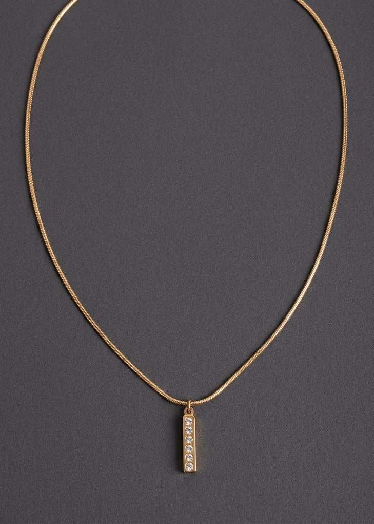 Anti tarnish gold chain necklace with a small vertical rectangular pendant featuring a row of clear stones, displayed on a dark gray background.