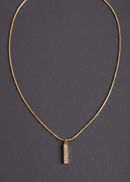 Anti tarnish gold chain necklace with a small vertical rectangular pendant featuring a row of clear stones, displayed on a dark gray background.