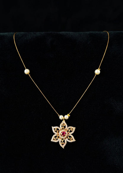 A gold necklace with a floral pendant and small pearl beads, displayed on a black velvet jewelry bust.