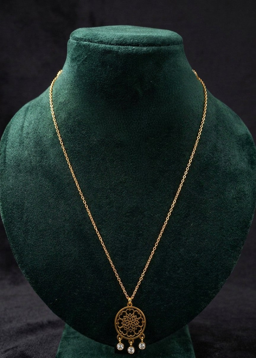 A gold-toned necklace with a circular filigree pendant and small dangling pearl-like beads, displayed on a dark green velvet jewelry bust against a black background.