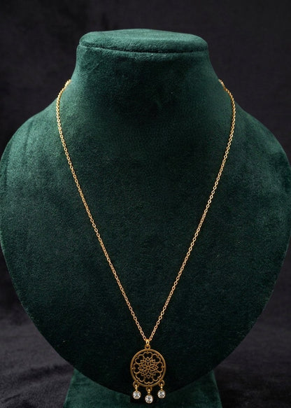 A gold-toned necklace with a circular filigree pendant and small dangling pearl-like beads, displayed on a dark green velvet jewelry bust against a black background.