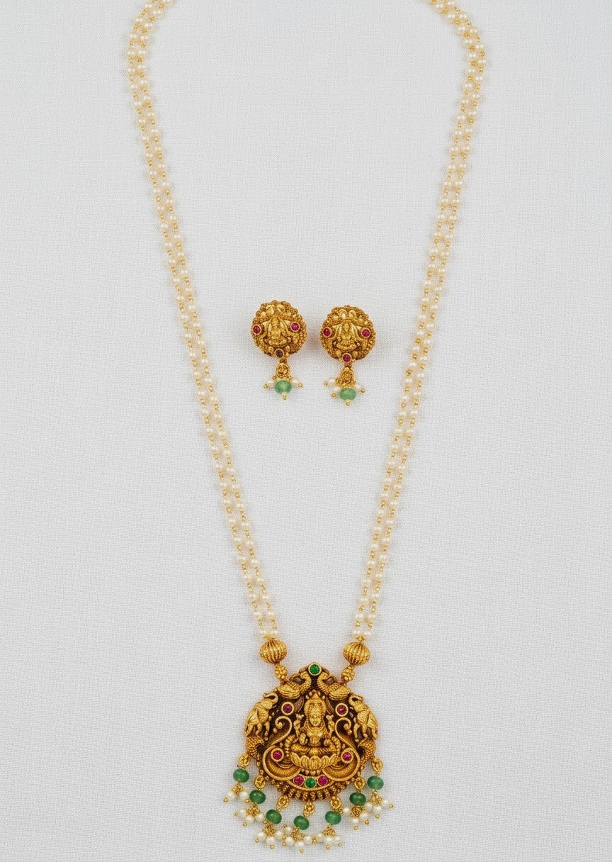 Gold-toned traditional necklace and matching earrings with green stone accents and small pearl-like bead details, displayed on a light neutral background.