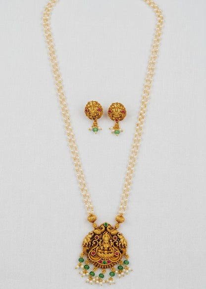 Gold-toned traditional necklace and matching earrings with green stone accents and small pearl-like bead details, displayed on a light neutral background.