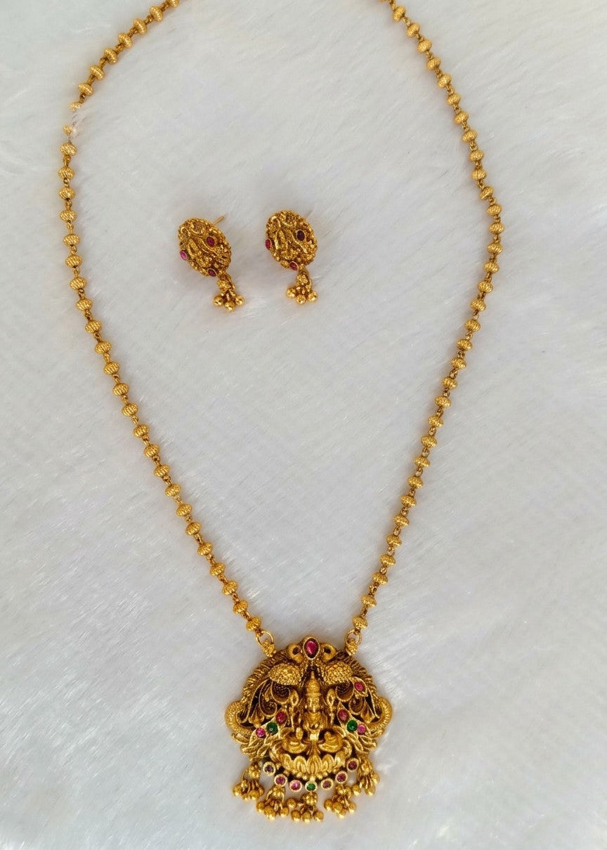 Gold necklace and matching stud earrings with an ornate decorative pendant, displayed on a white textured background.