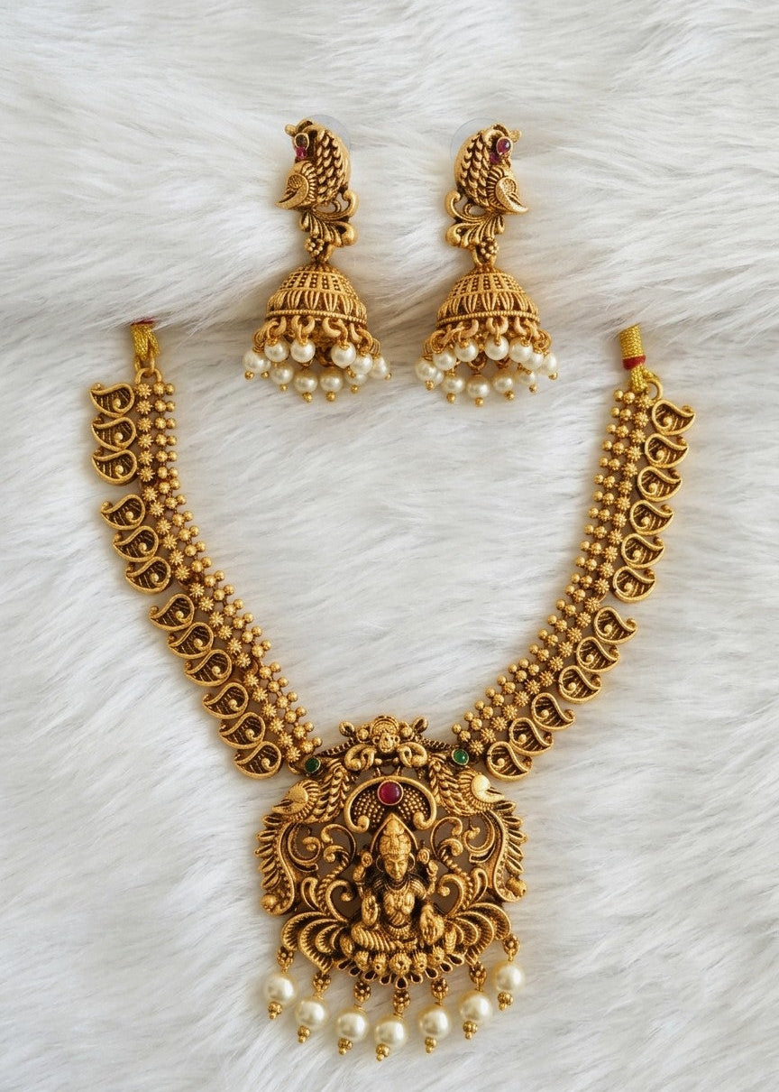 Gold-toned traditional Indian jewelry set featuring a necklace with a detailed Lakshmi pendant, matching earrings, and pearl accents, arranged on a white faux fur background.