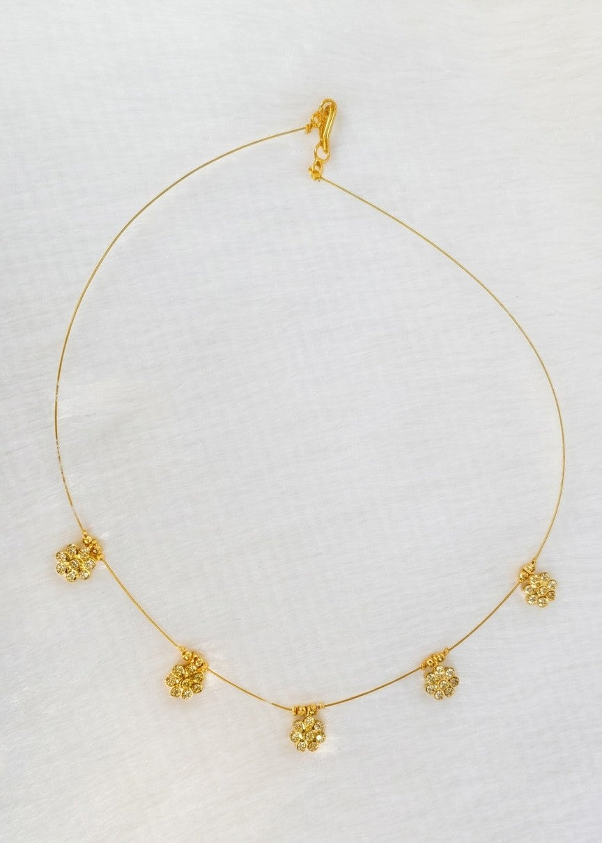 A delicate gold chain necklace with five small, textured gold floral or cluster charms spaced along the chain, displayed on a textured white fabric background.