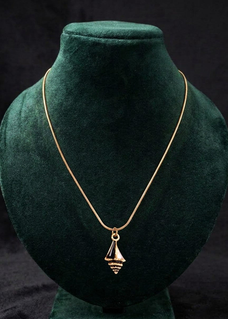 A gold chain necklace with a small geometric pyramid pendant, displayed on a dark green velvet jewelry bust against a black background.