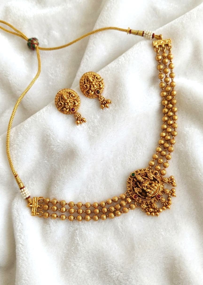 Gold-toned traditional necklace and matching earrings displayed on a soft white fabric background.
