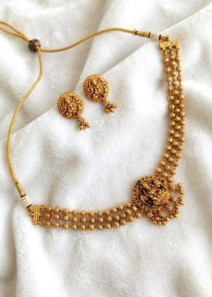 Gold-toned traditional necklace and matching earrings displayed on a soft white fabric background.