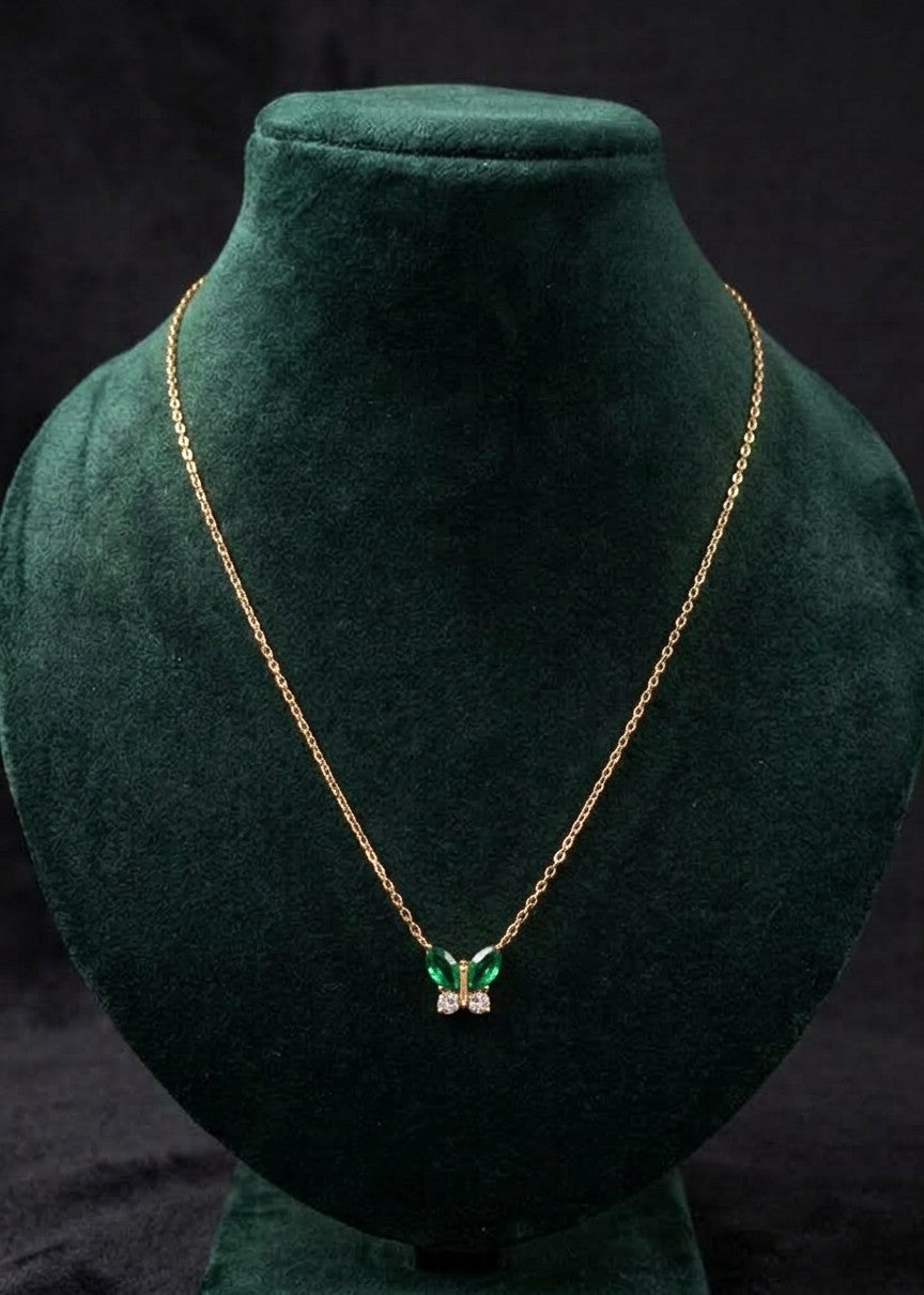 Faye gold-toned butterfly necklace with green stone wings and clear crystal accents on a dark green display bust.