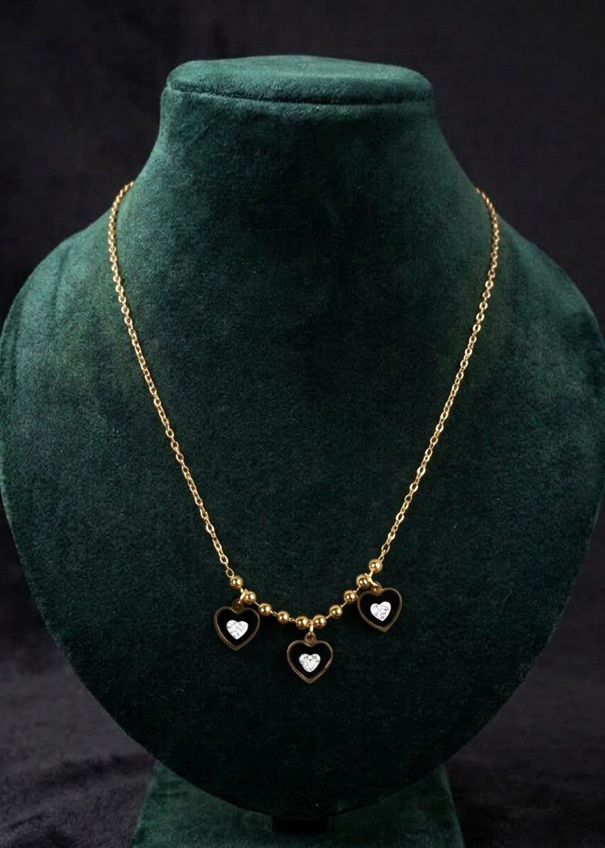 A gold chain necklace with three small heart charms, displayed on a dark green velvet jewelry bust against a black background.