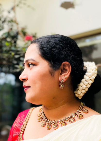 A woman in profile wearing traditional Indian jewelry, including a gold-toned necklace, earrings, 