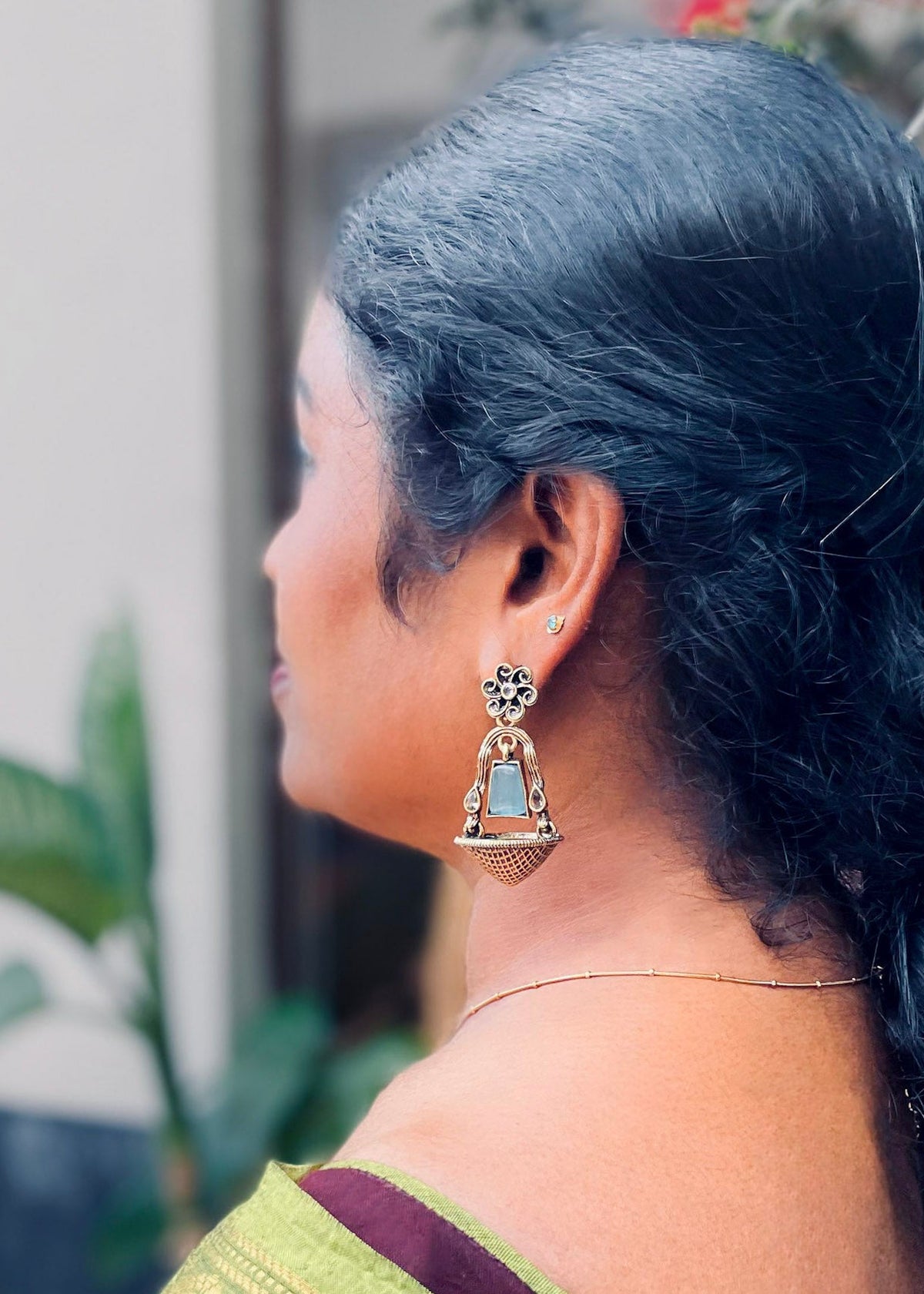 A woman shown from the side profile wearing a gold-toned traditional Indian earring with a light blue stone, 