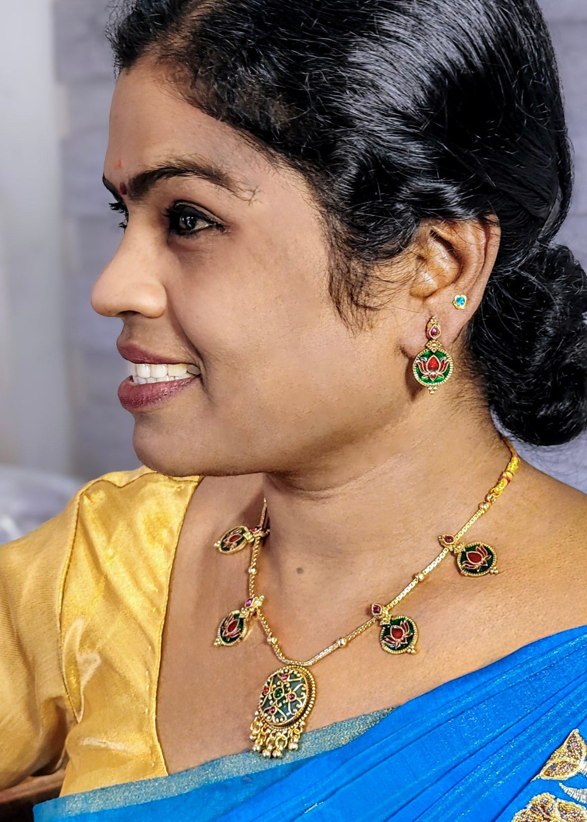 A woman wearing an Antique style necklace set with green enamel pendant and red lotus engraved in green enamel accents. Pairing earring of the same accent