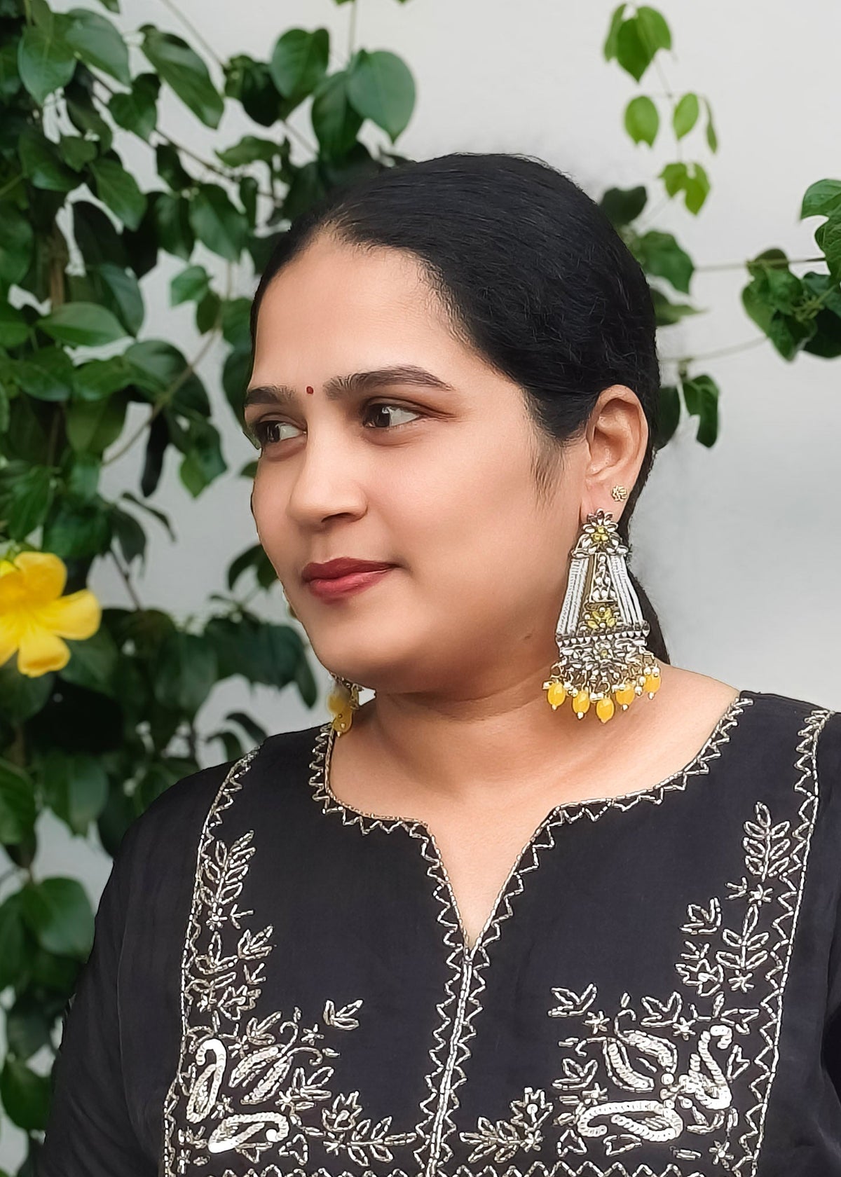 A woman wearing a large silver and yellow jhumka earrings.
