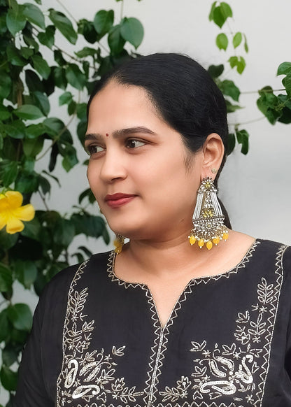 A woman wearing a large silver and yellow jhumka earrings.