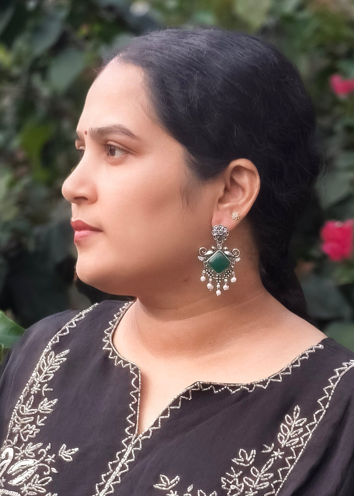 A woman in profile wearing a silver-toned earrings with green stones.