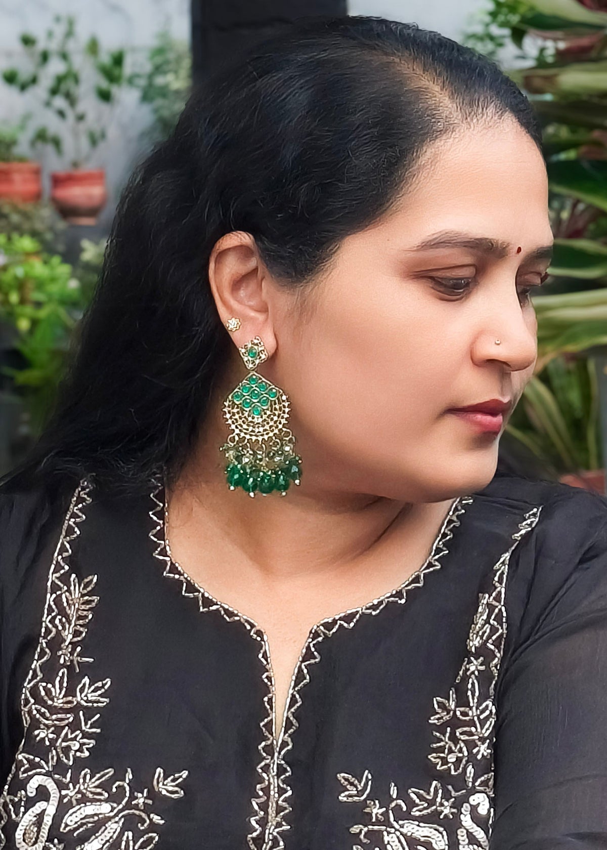 A woman wearing a large green and gold jhumka earring.