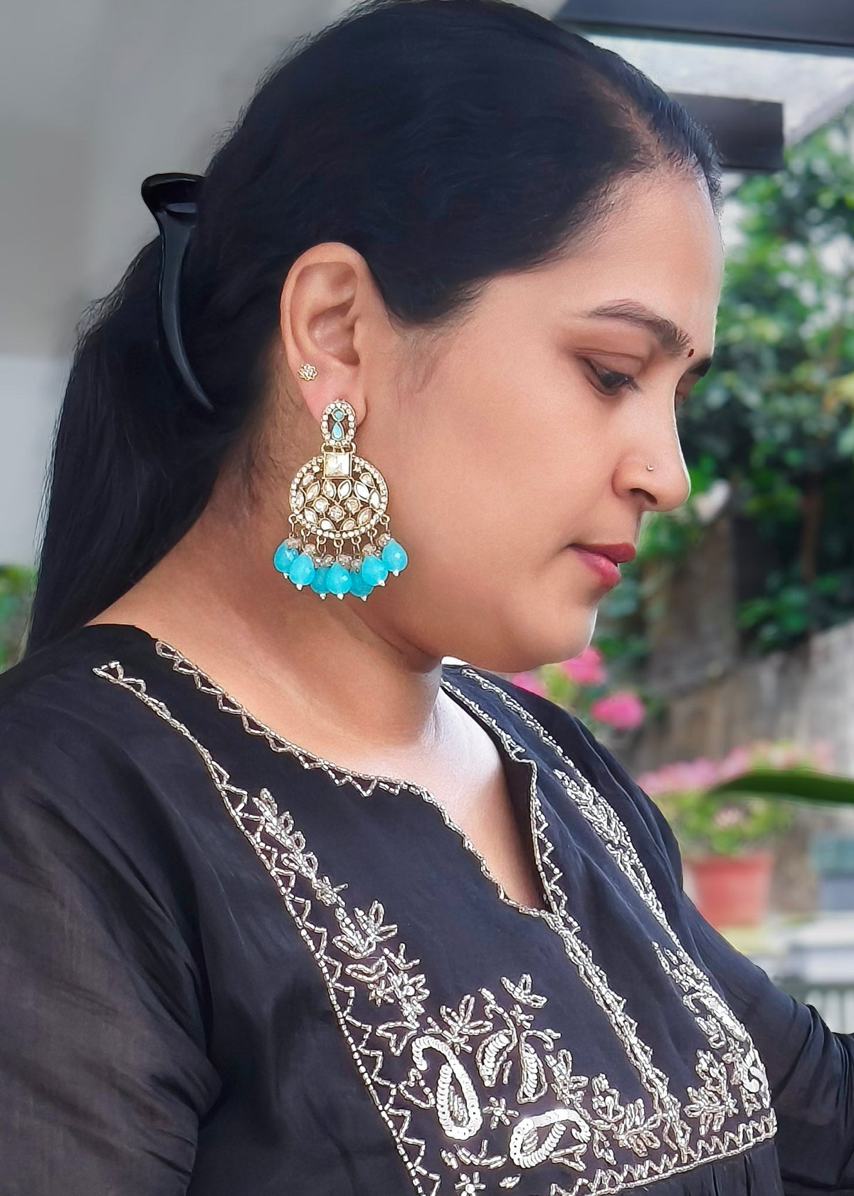 A woman wearing a large gold-toned jhumka earring with turquoise blue beads.