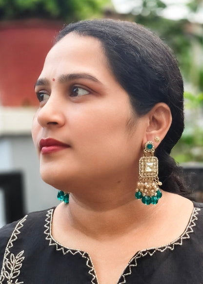 A woman wearing ornate gold-toned dangle earrings with green bead accents .