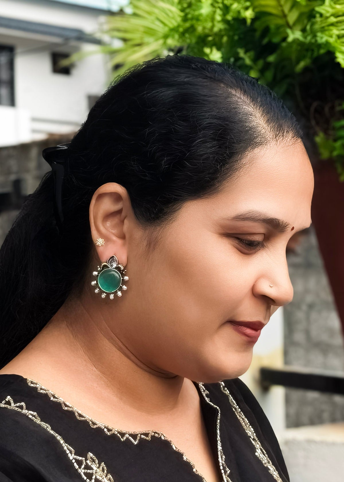 A woman in profile wearing a silver-toned earring with a turquoise blue stone and white crystal border.