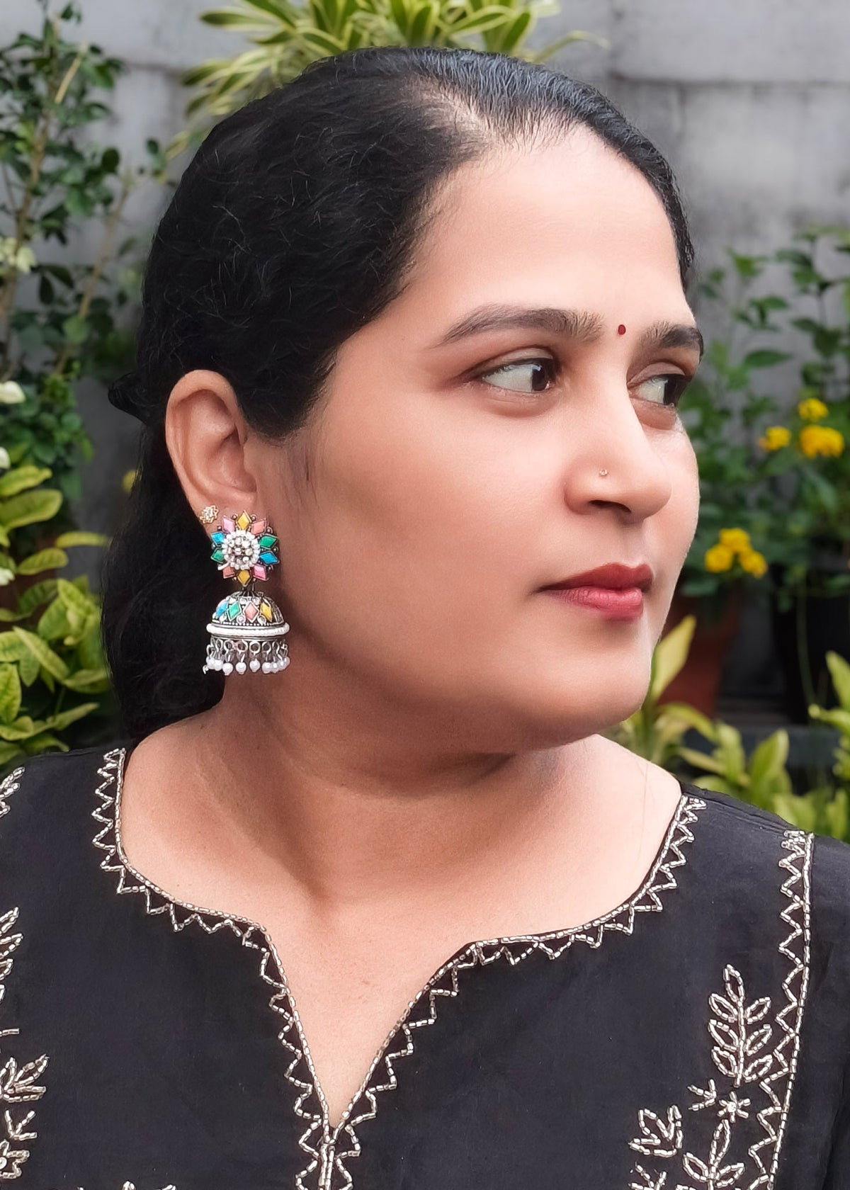 A woman wearing a colorful, ornate silver-toned jhumka earring.